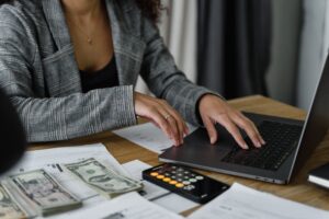 A woman with a laptop, ledger and cash managing finances through divorce using our tips.