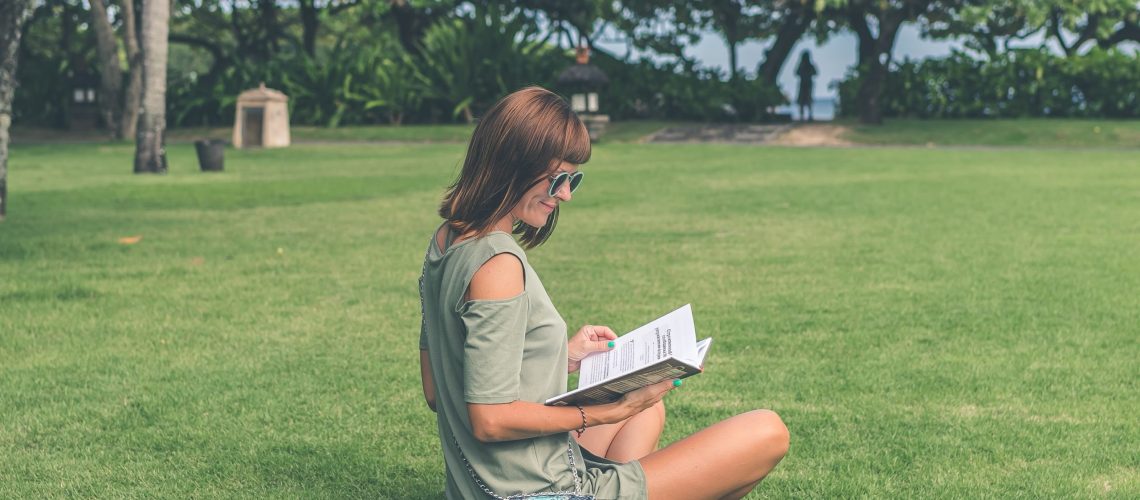 A woman reading a book in a grassy spot is perhaps perusing one of our beach picks for books for divorced women
